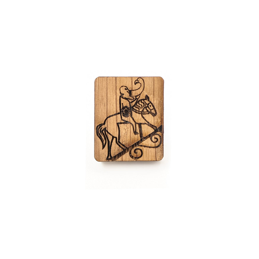A rectangular wooden pin badge with a design taken from a Pictish carving of a man drinking whilst riding a horse burned onto it.