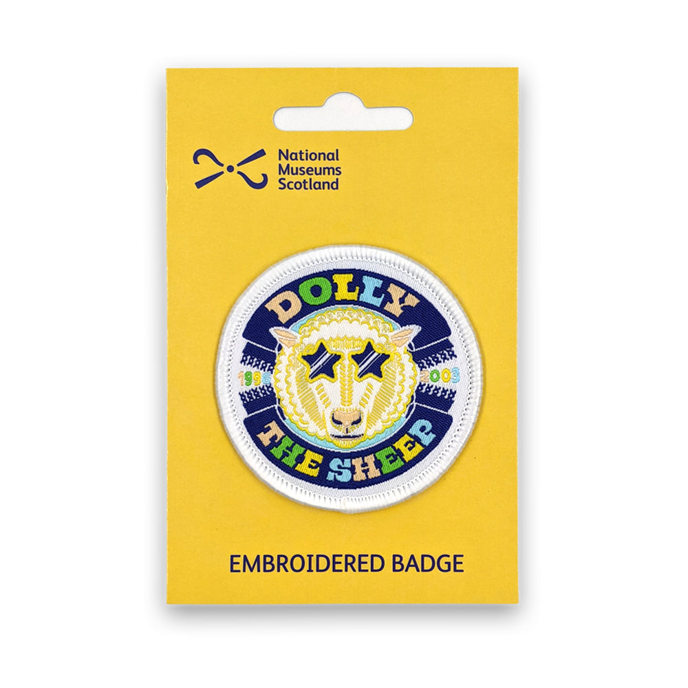 A round embroidered patch with a colourful design of Dolly the sheep on a yellow backing card against a plain white background.