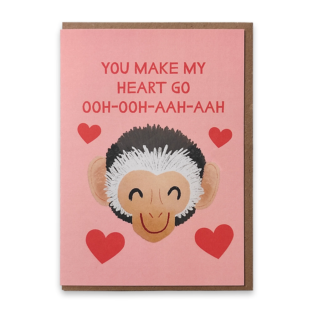 A photograph of a greetings card with an illustration of a smiling monkeys face surrounded by red love hearts, above the monkey's face are the words "You make my heart o ooh ooh aah aah" in red.