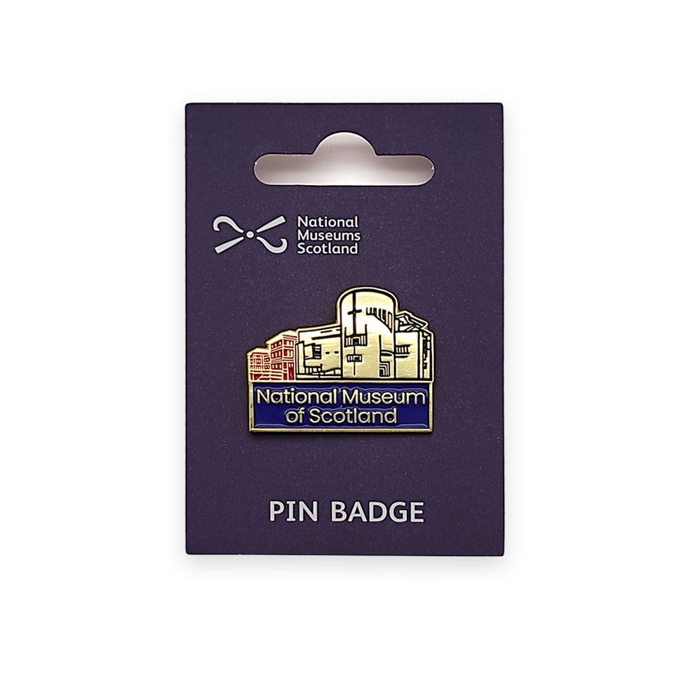 A metallic pin badge with an image of the national museum of Scotland on a navy backing card. The pin badge and the backing are against a plain white background.