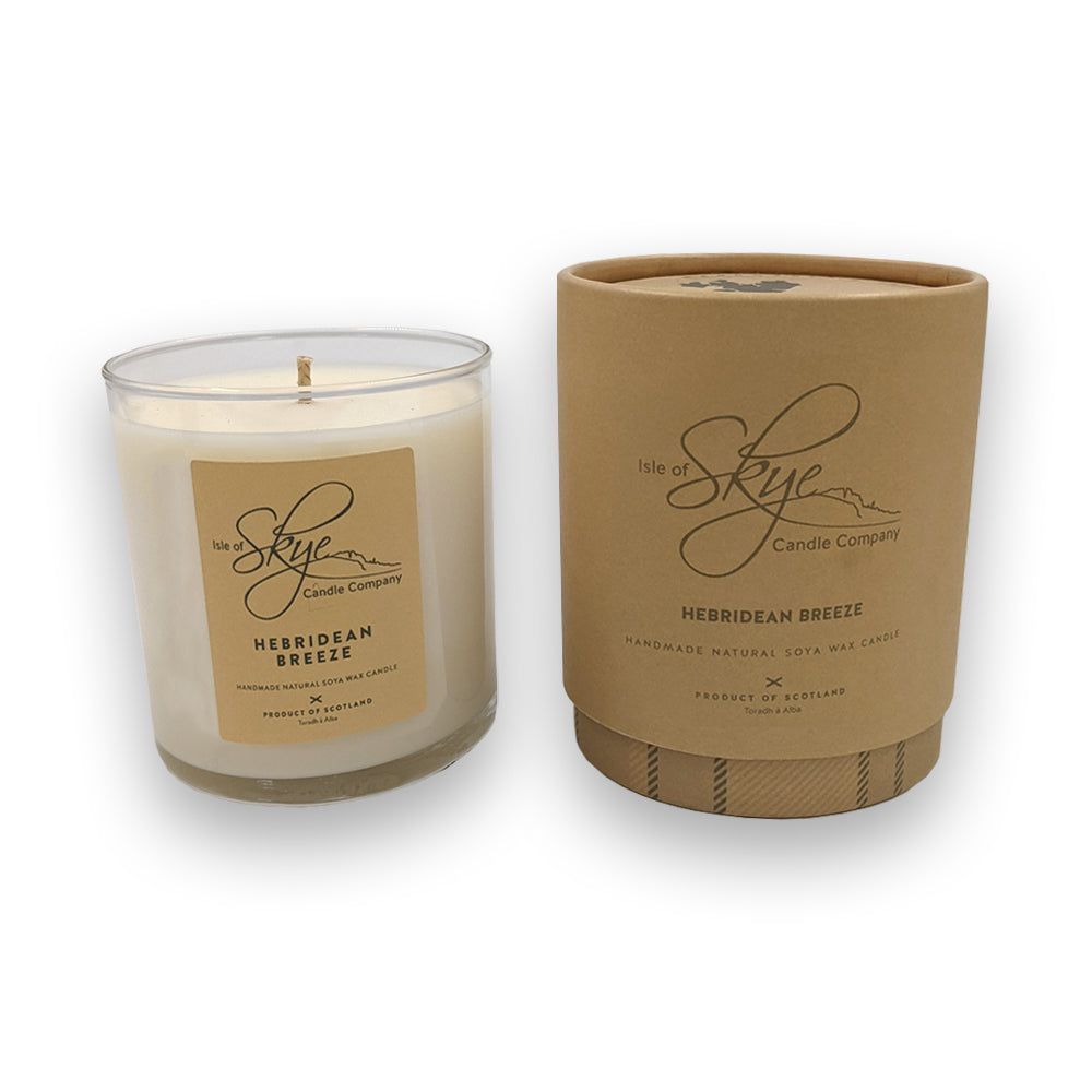 A candle in a glass holder to the left of a round beige box against a plain white background.