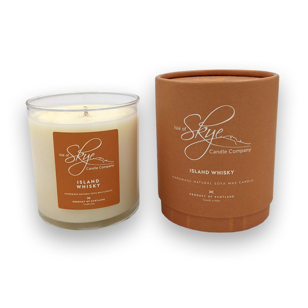 A candle in a glass holder to the left of a round orange box against a plain white background.