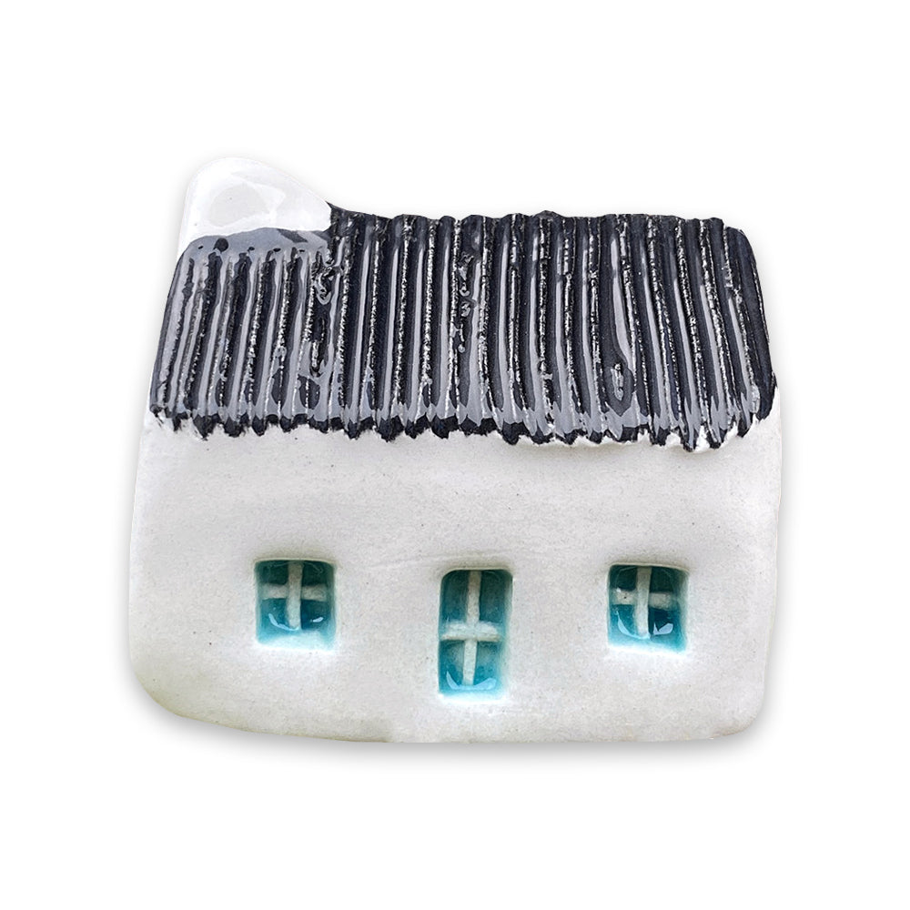 A small white ceramic cottage with a black painted roof and a blue door and windows against a plain white background.