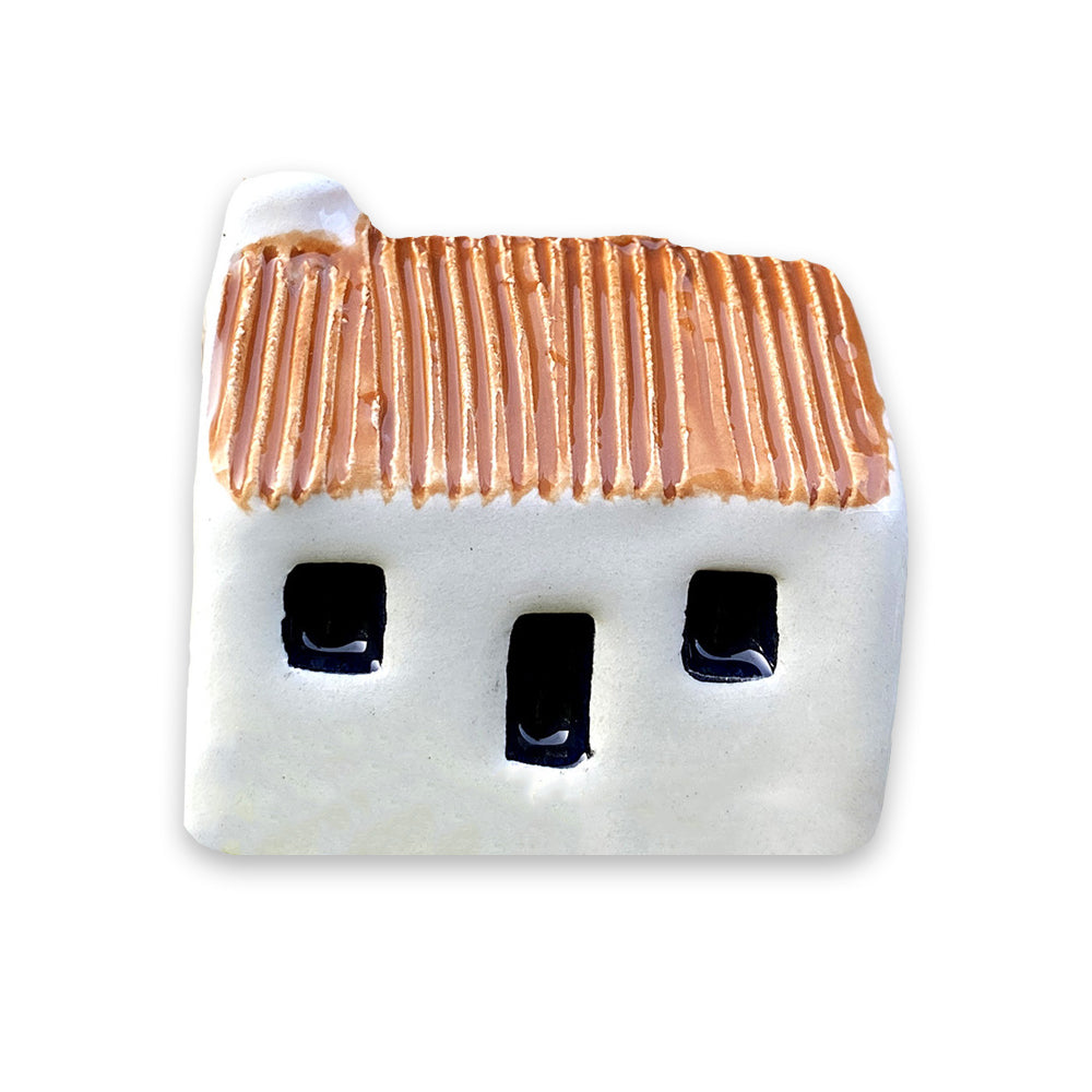 A small white ceramic cottage with a brown painted roof and a black door and windows against a plain white background.