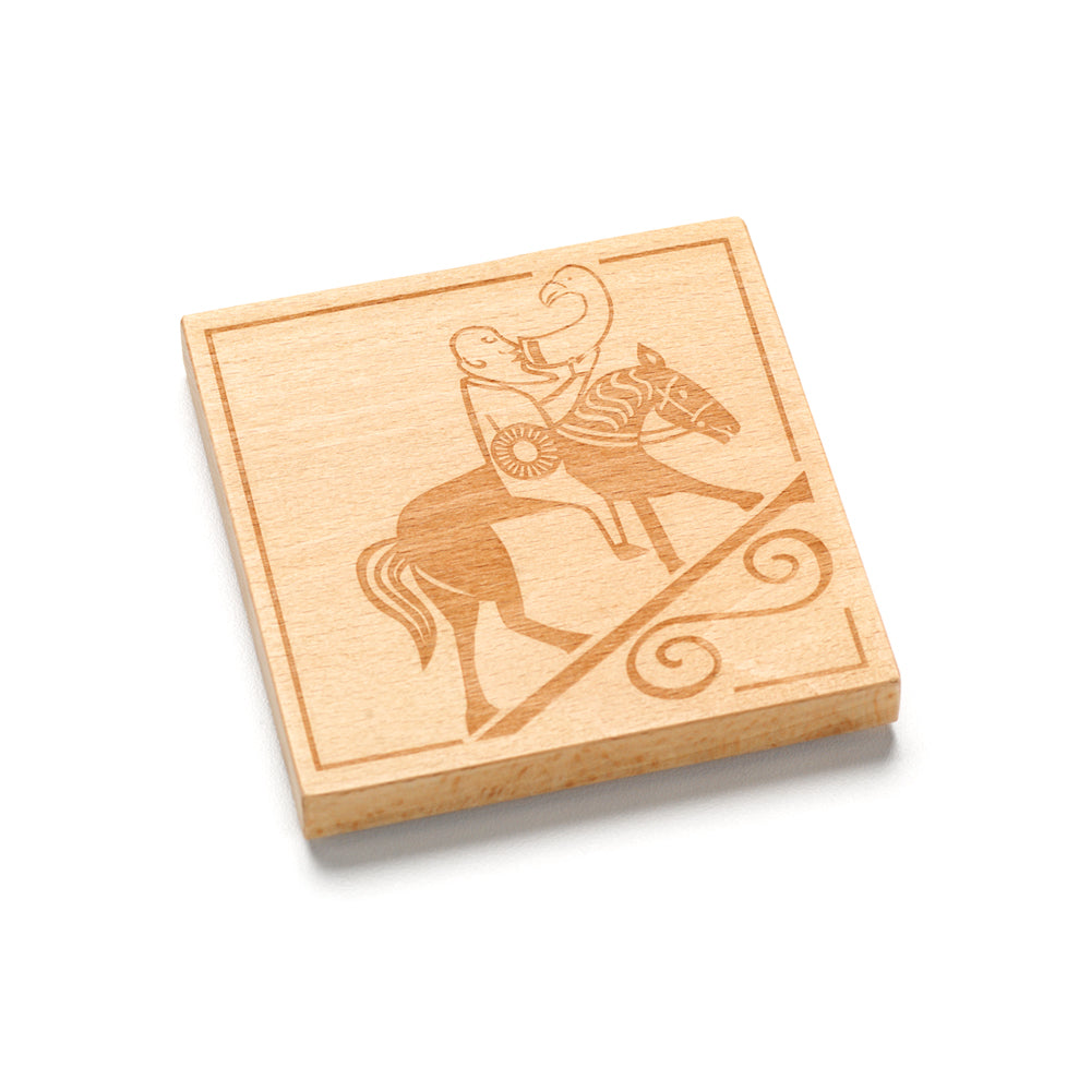 A square wooden coaster with a design taken from a Pictish carving of a man drinking whilst riding a horse carved into it.