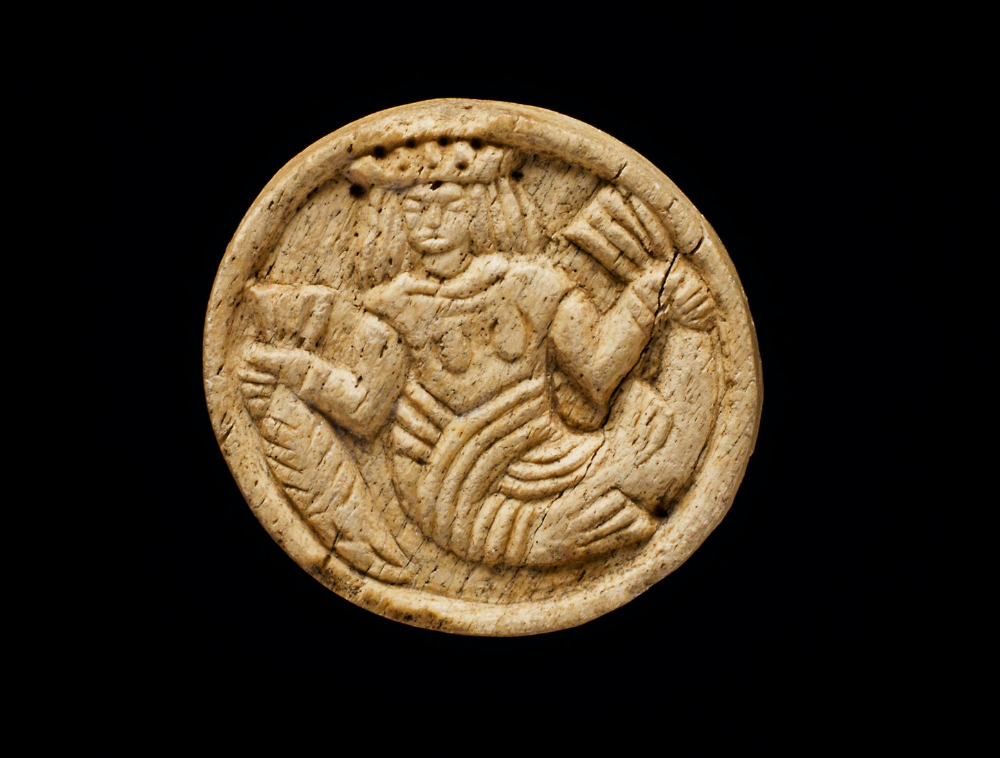An ivory game counter from the 15th or 16th century found on Iona. The round counter has a mermaid wearing a crown and holding a larger fish by the tail in each hand.