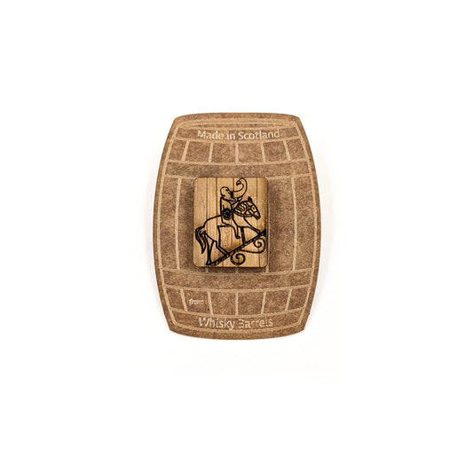 A wooden rectangular pin badge with a design of a man drinking on a horse burned onto it. The pin badge is mounted on a brown backing card in the shape of a barrel .