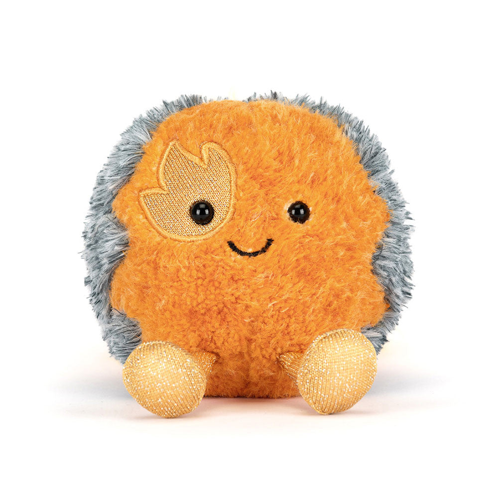 A soft toy of a flaming comet with a smiley face, yellow legs and an orange fluffy trail of faire against a white background.