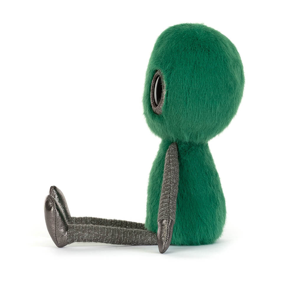 Side view of a soft toy of a green alien with large black eyes against a white background.