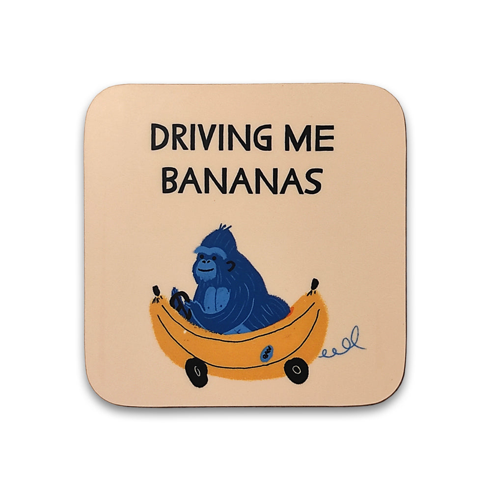 A photograph of a yellow coaster against a plain white background. The coaster is printed with an illustration of a blue gorilla driving a banana shaped car, the words "driving me bananas" are printed above.