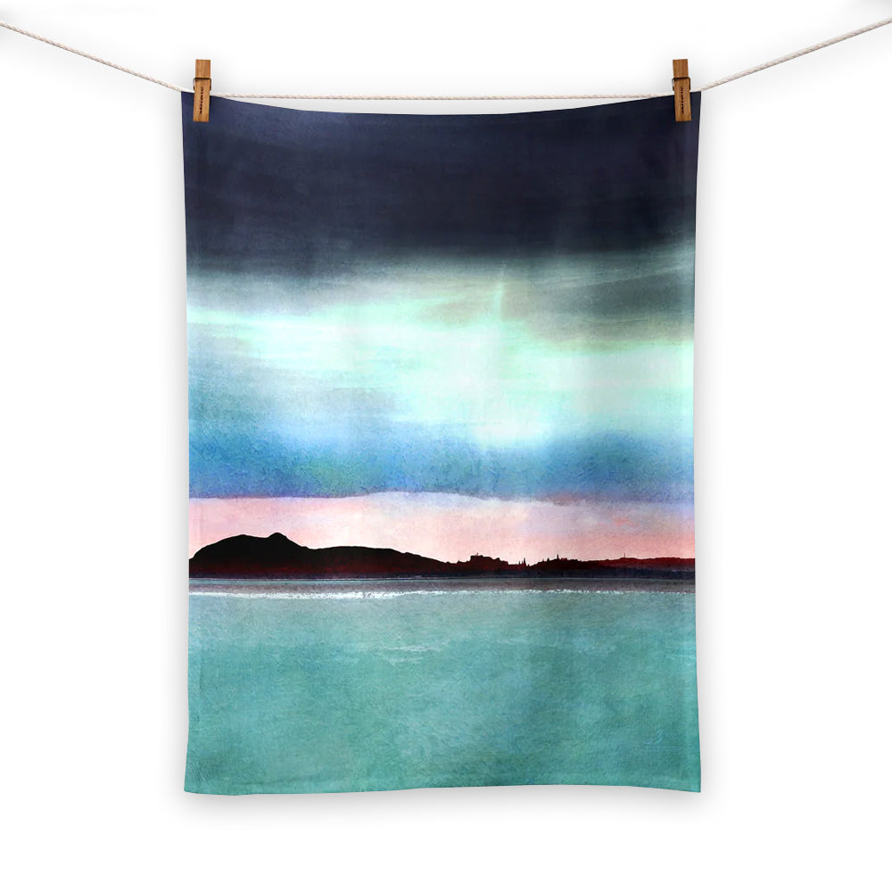 Tea towel with a watercolour painting of Edinburgh's skyline silhouetted over a pink sunset.