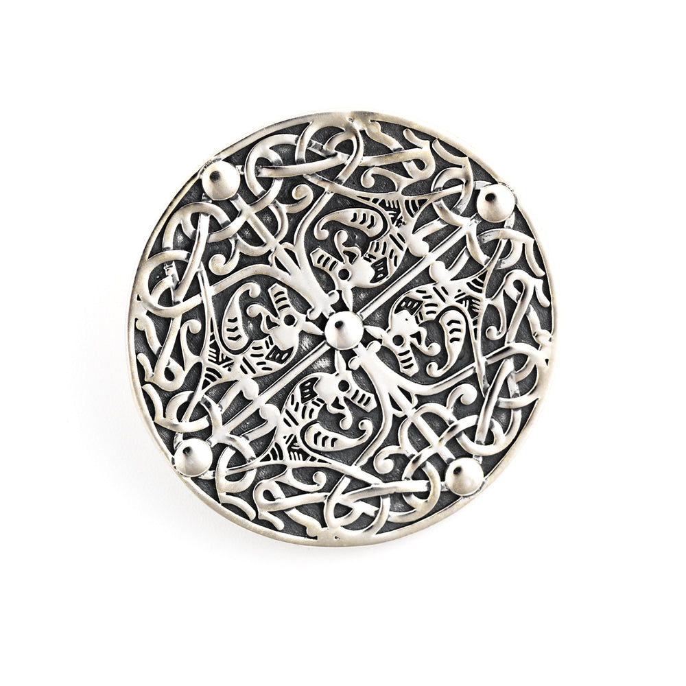 A round silver brooch, with a four way symmetrical design of four beasts,intertwined with vegetation, against a plain white background