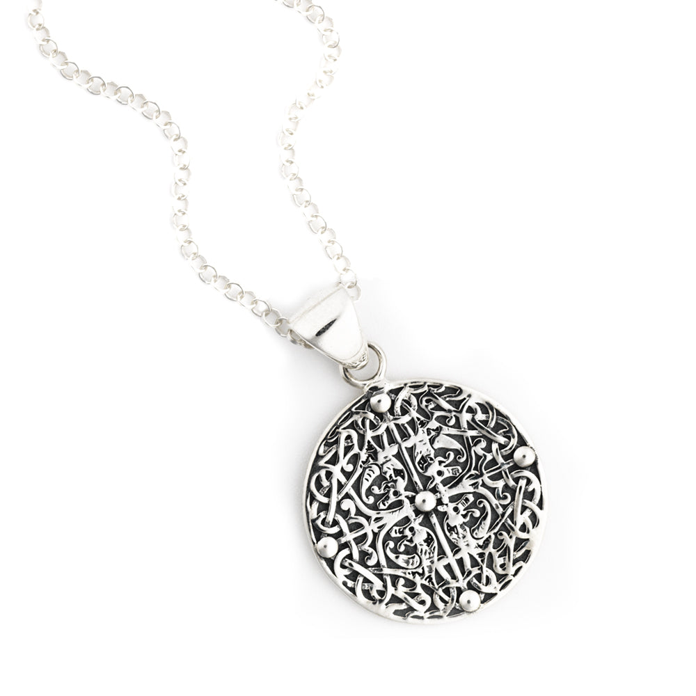 A round silver pendant, with a four way symmetrical design of four beasts, intertwined with vegetation, against a plain white background.