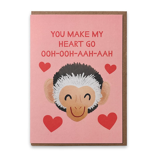 A photograph of a greetings card with an illustration of a smiling monkeys face surrounded by red love hearts, above the monkey's face are the words "You make my heart o ooh ooh aah aah" in red.