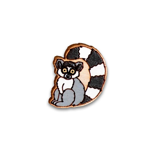 A wooden cartoon lemur pin badge against a plain white background. The Lemur is painted in grey, white, and black.