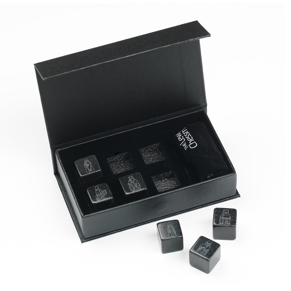 A black box with an open lid. Inside are three whisky stones with etchings of the Lewis Chess Pieces, three more whisky stones sit beside the box.