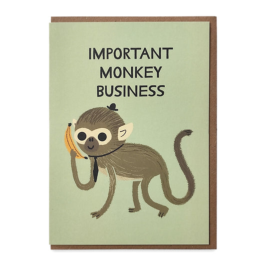 A photograph of a greetings card with an illustration of a monkey wearing a hat and tie and holding a banana to its ear like a phone, above it are the words "important monkey business"