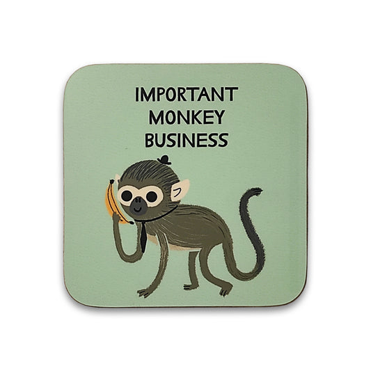 A photograph of a pale green square coaster against a plain white background. The coaster is printed with an illustration of a monkey in a hat and tie holding a banana like a phone. Above the monkey are the words "important monkey business".