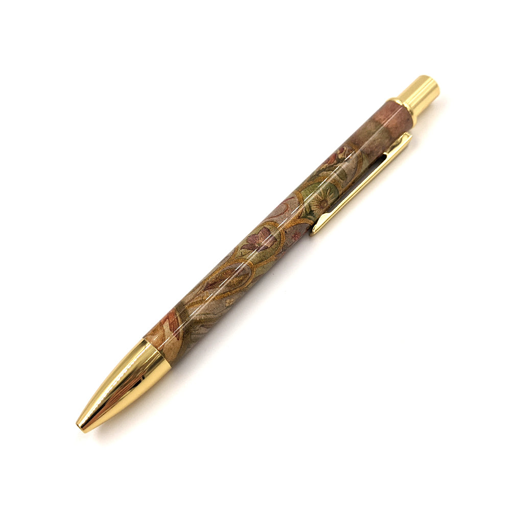 A retractable metal pen with a gold coloured tip and clicker. The shaft of the pen is decorated with a floral detail from the 'Willowwood Piano' by Phoebe Anna Traquair.
