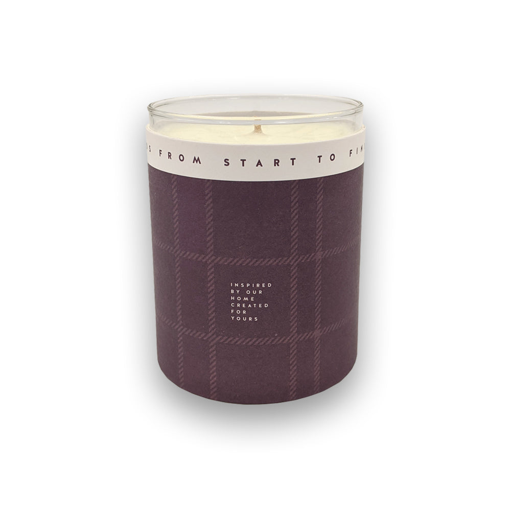 A candle in a glass holder and purple casing against a plain white background.