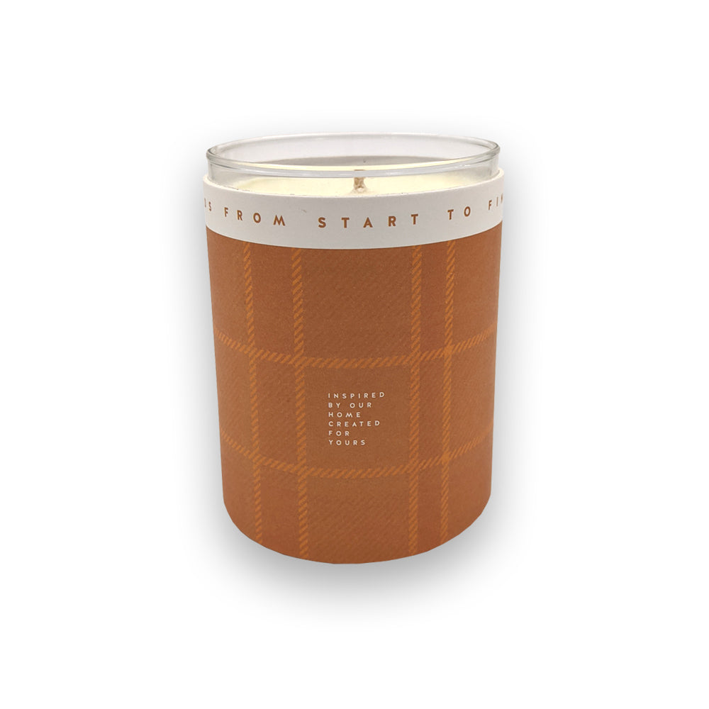 A candle in a glass holder and orange casing against a plain white background.