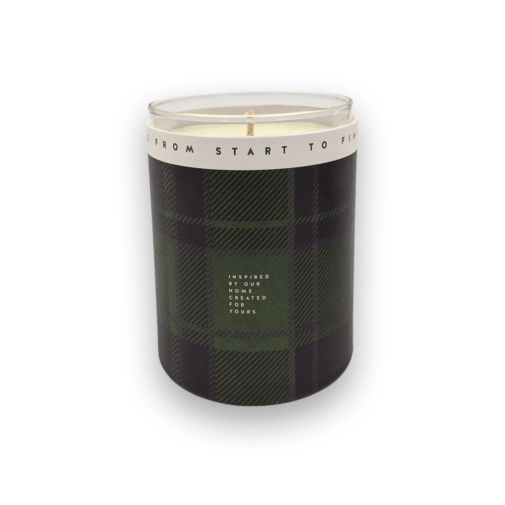 A candle in a glass holder and green casing against a plain white background.