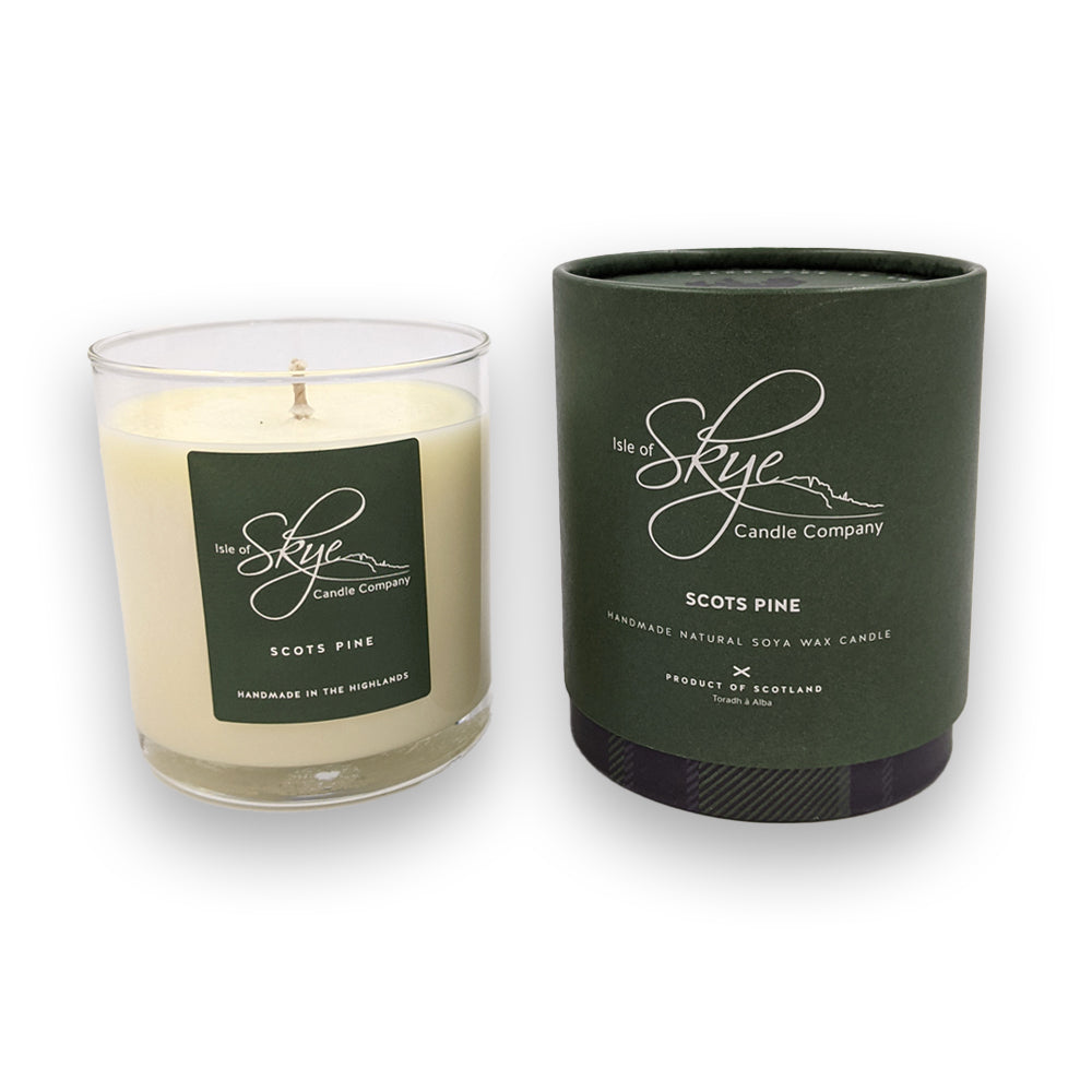 A candle in a glass holder to the left of a round green box against a plain white background.