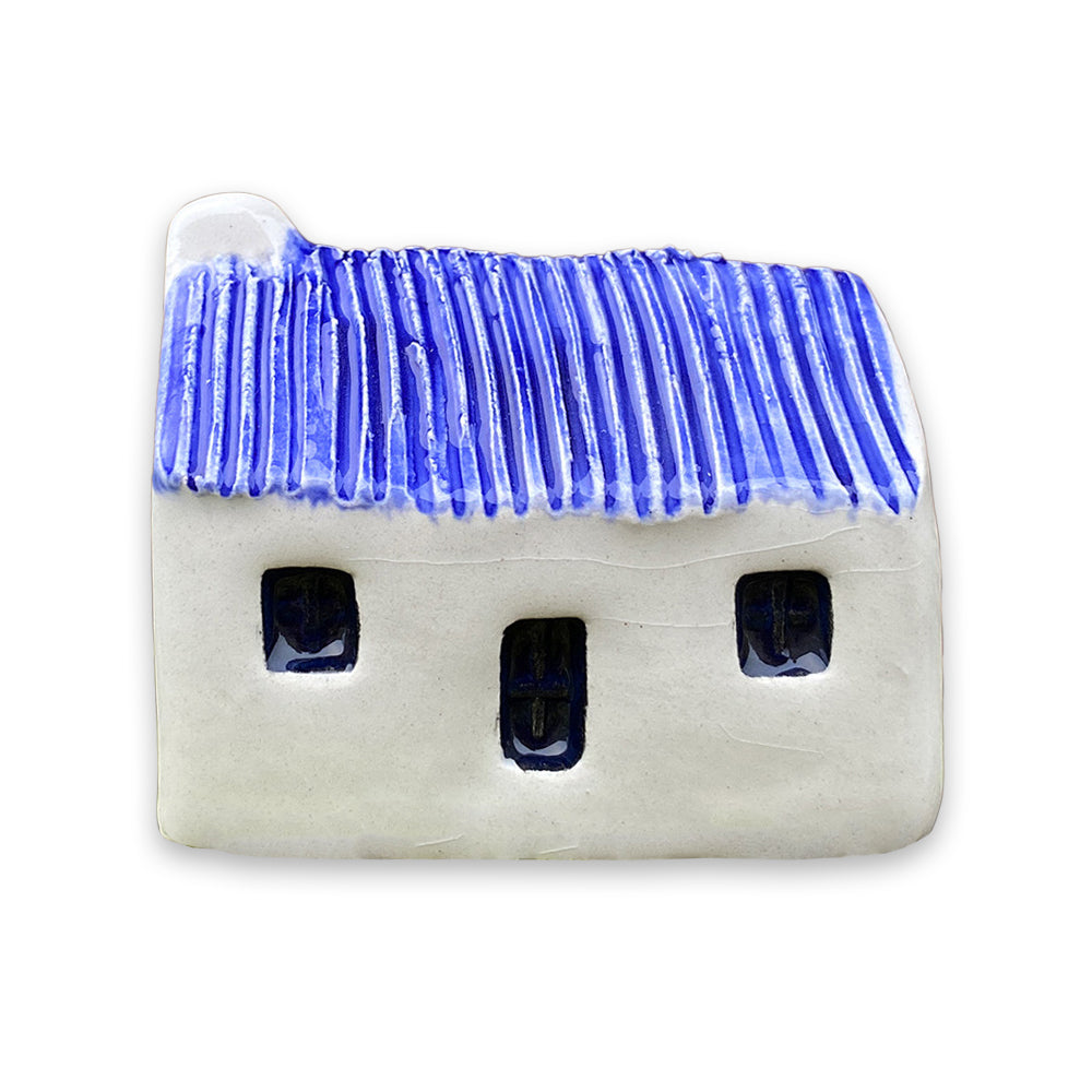 A small white ceramic cottage with a blue painted roof and a black door and windows against a plain white background.
