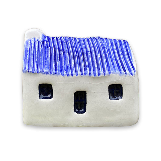 A small white ceramic cottage with a blue painted roof and a black door and windows against a plain white background.
