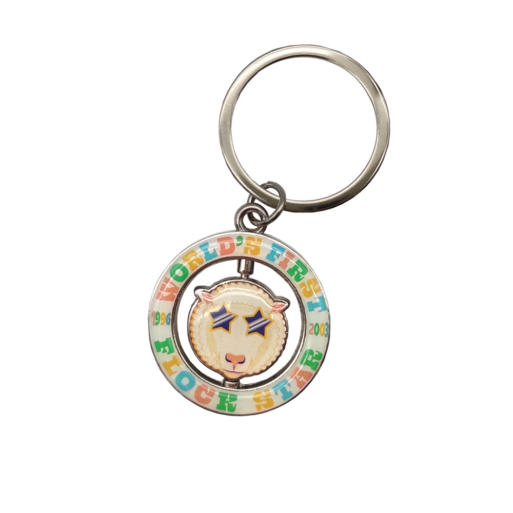 A white ring keyring with the words 'Dolly the sheep' in various colours round it. In the centre of the ring is a spinning Dolly the sheep's face.
