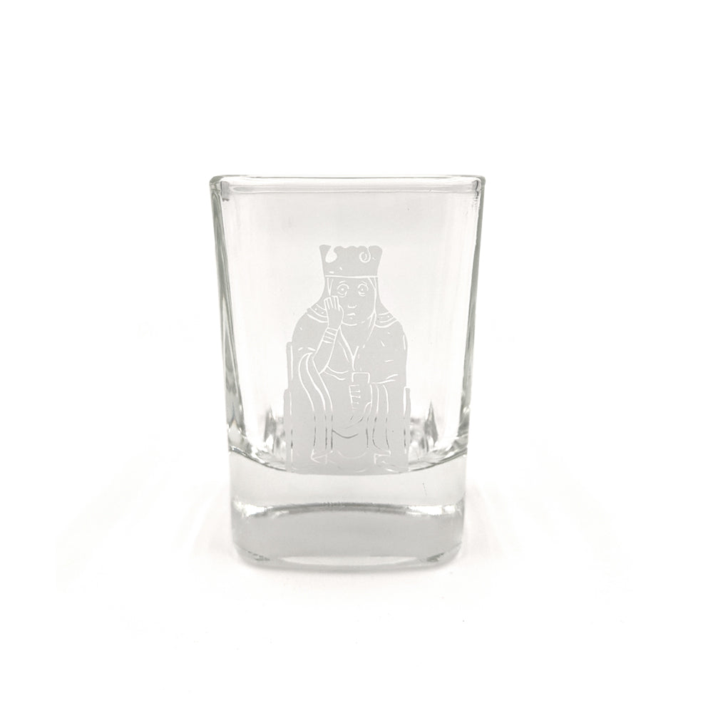 A rounded square shot glass with a printed illustration of a queen Lewis chess piece in grey.