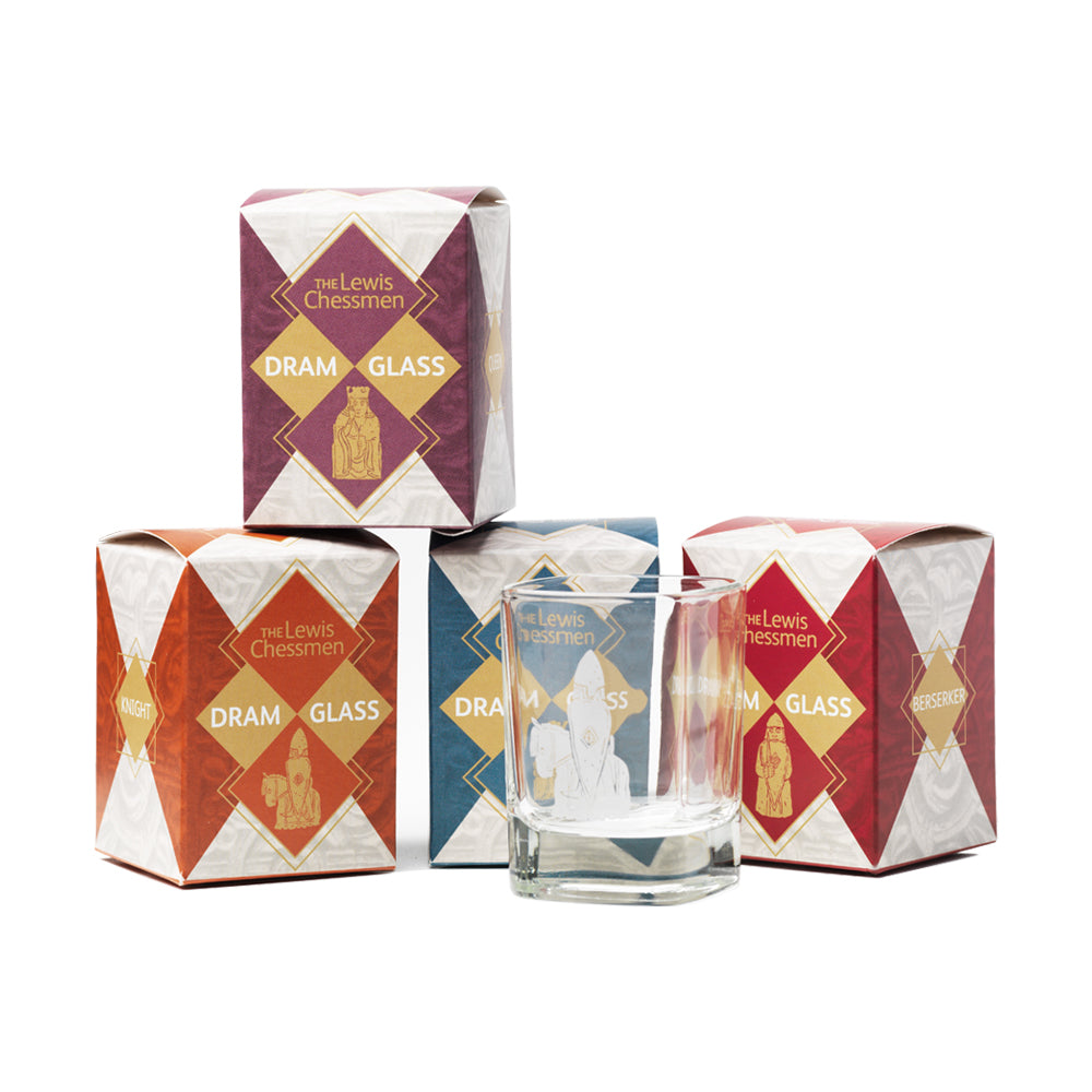 A photograph of three cardboard boxes with a fourth sat on top of them. The boxes each have a different colour. Red for berserker, orange for knight, purple for queen, and blue for king. A rounded square shot glass with a printed illustration of a knight Lewis chess piece sits in front.