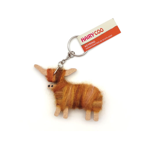 A keyring shaped like a highland cow made from orange wool and wood against a plain white background