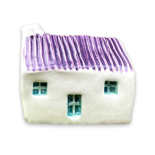 A small white ceramic cottage with a purple painted roof and a blue door and windows against a plain white background.