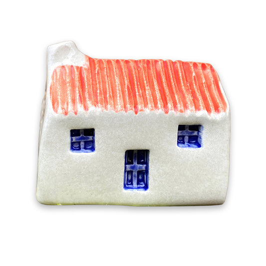 A small white ceramic cottage with a red painted roof and a blue door and windows against a plain white background.