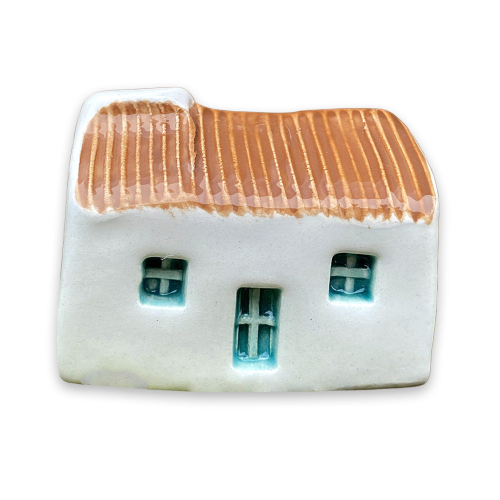 A small white ceramic cottage with a brown painted roof and a blue door and windows against a plain white background.
