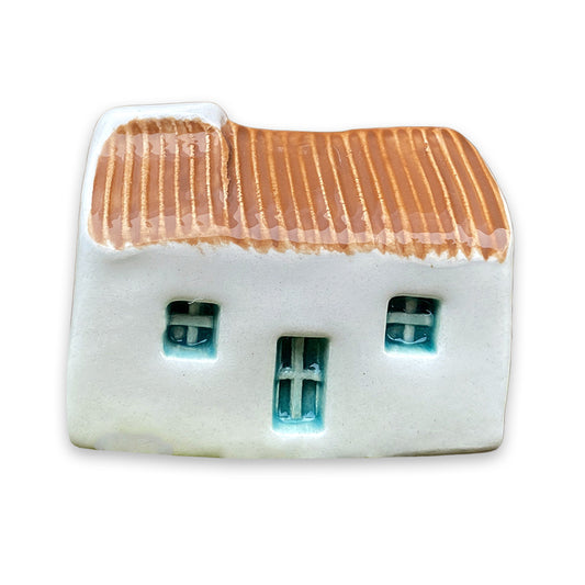 A small white ceramic cottage with a brown painted roof and a blue door and windows against a plain white background.