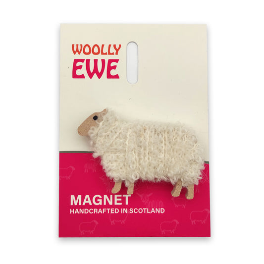 A magnet of a sheep made from wood and white wool on a white and pink backing card.