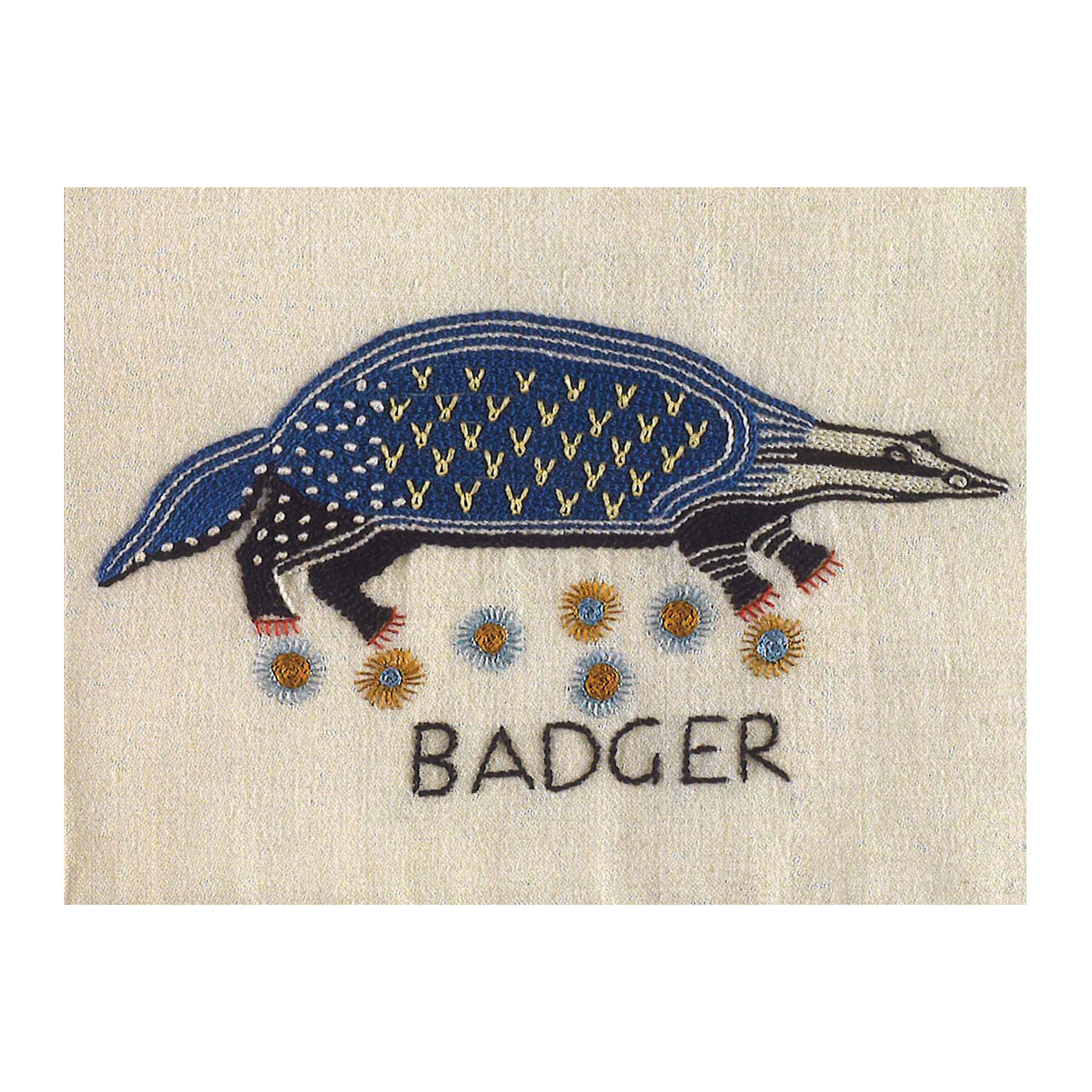 Greetings card with a photograph of an embroidered badger. The badger is embroidered in black and blue thread and is stood above a patch of flowers, the word "badger" is embroidered beneath.
