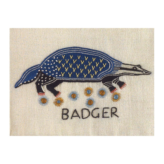 Greetings card with a photograph of an embroidered badger. The badger is embroidered in black and blue thread and is stood above a patch of flowers, the word "badger" is embroidered beneath.