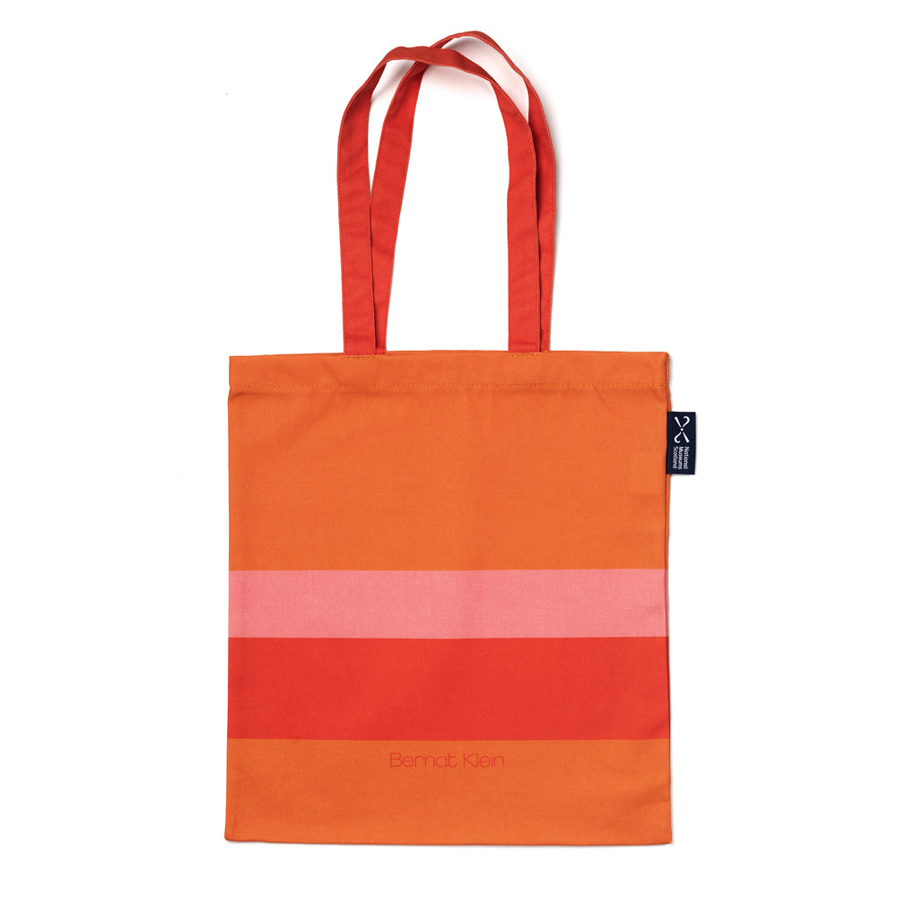 An orange and pink striped cotton shopping bag based on Bernat Klein's work against a plain white background.