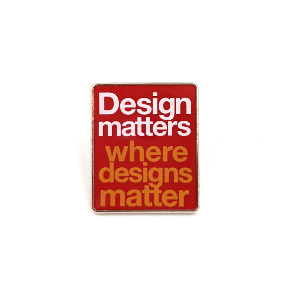 A rectangular pin red pink badge against a plain white background. Text on the badge reads "Design matters where designs matter", a quote by Bernat Klein.