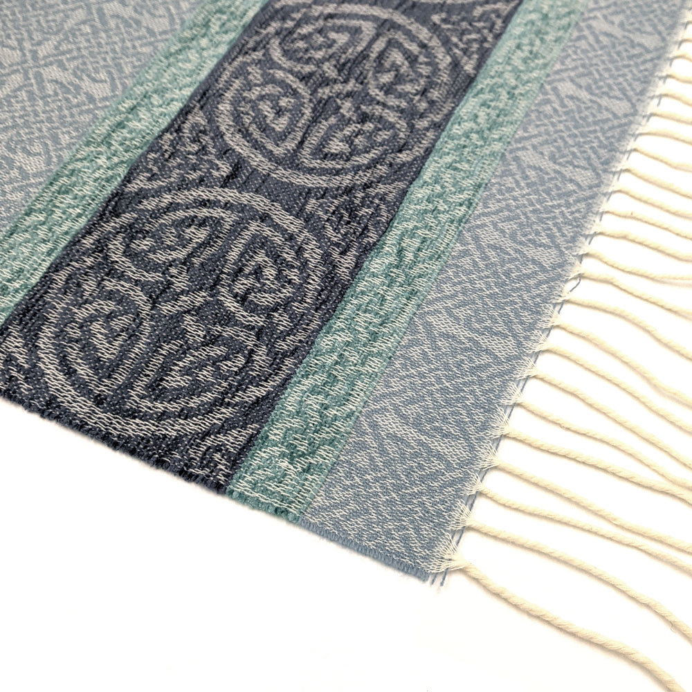 Pale blue tassled scarf detail with a celtic roundal pattern against a plain white background.