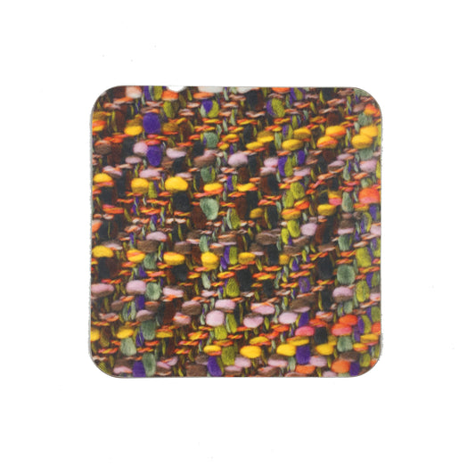 A square coaster with a photograph of the Bernat Klein fabric "Festival". The fabric is woven in yellows, greens, browns, and purples.