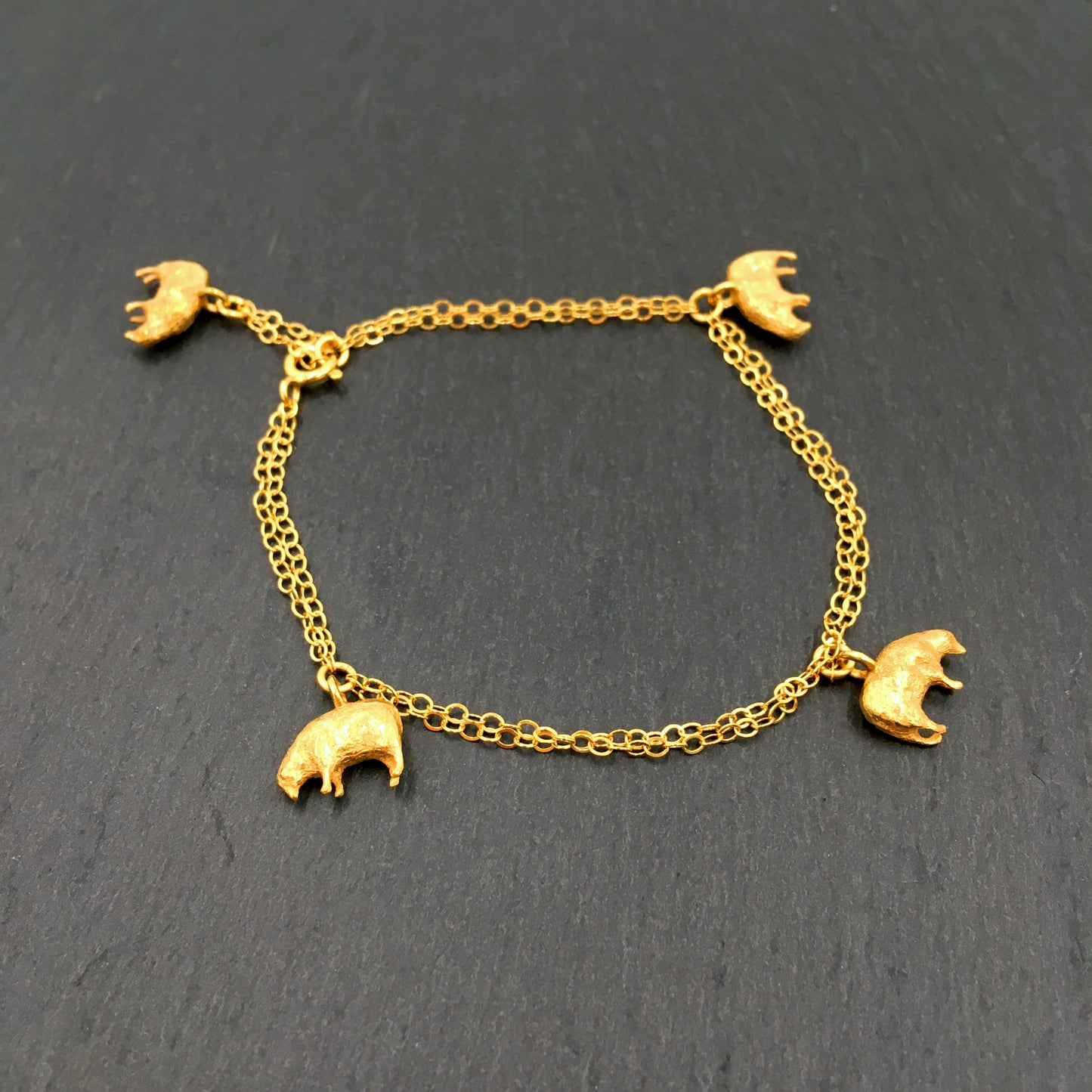 A gold plated bracelet with four sheep charms against a slate background.