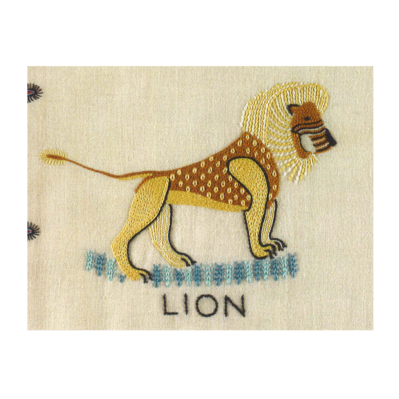A horizontal rectangular greetings card with a photograph of an embroidered lion. The lion is embroidered in yellows and browns against a plain cream fabric background. Underneath the lion is the word "lion" embroidered in black.