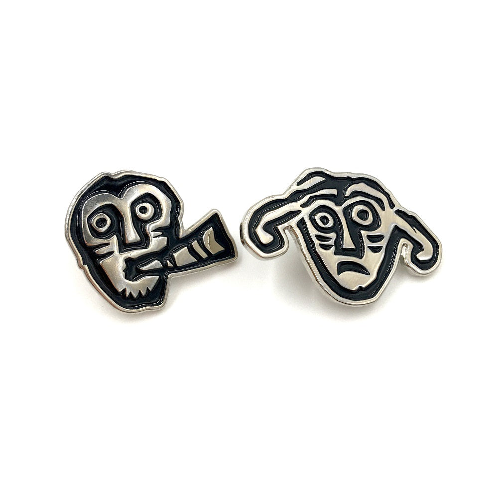 two pin badges with faces from a detail of a brooch from the Galloway hoard. A face with a worried look and two large droopy ears and face playing a horn.