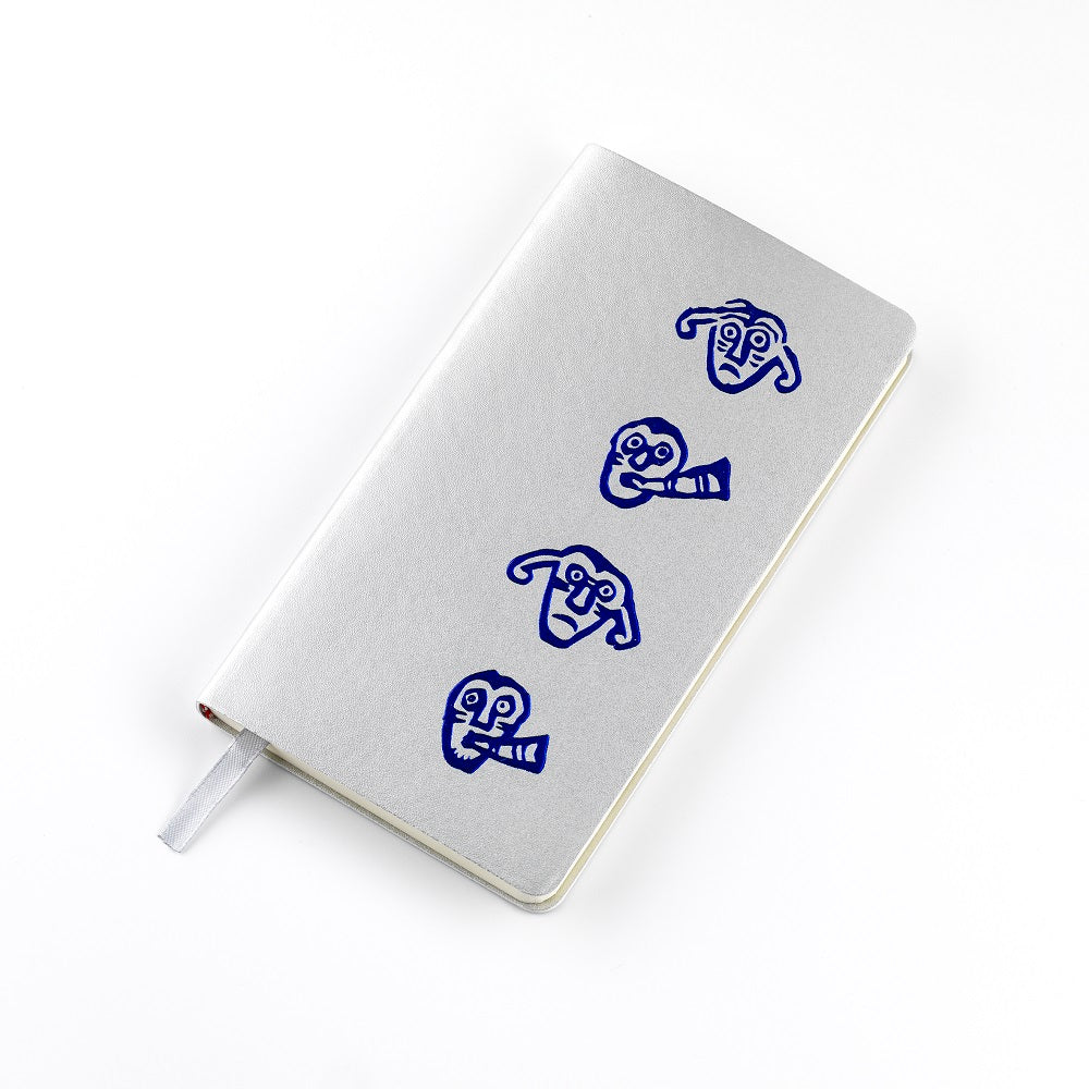 A silver imitation leather bound notebook with a blue embossed design of a faces from a detail of a brooch from the Galloway hoard.