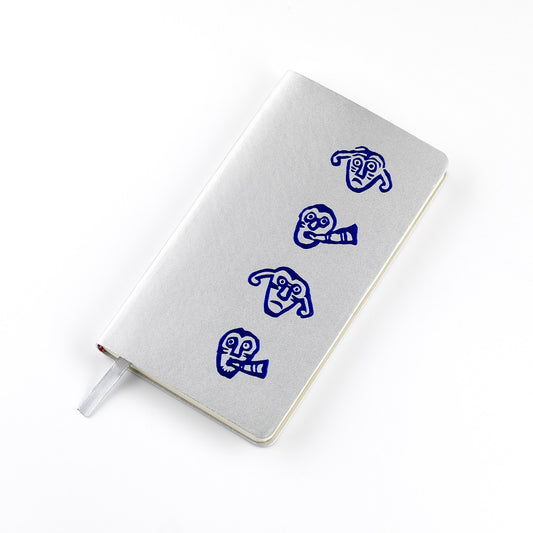 A silver imitation leather bound notebook with a blue embossed design of a faces from a detail of a brooch from the Galloway hoard.