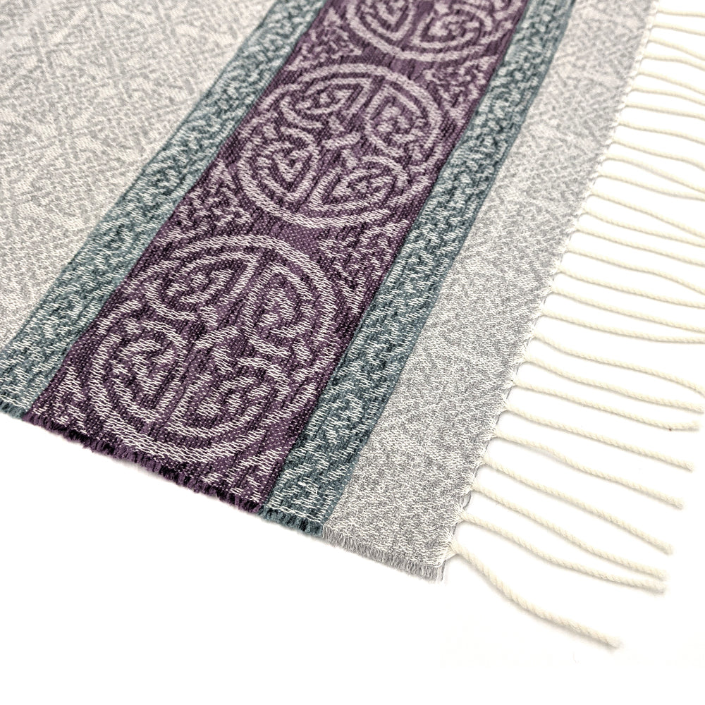 Grey tassled scarf detail with a purple celtic roundal pattern against a plain white background.